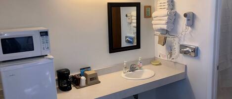 Baño de hotel con lavamanos blanco, microondas, cafetera y secador de pelo.