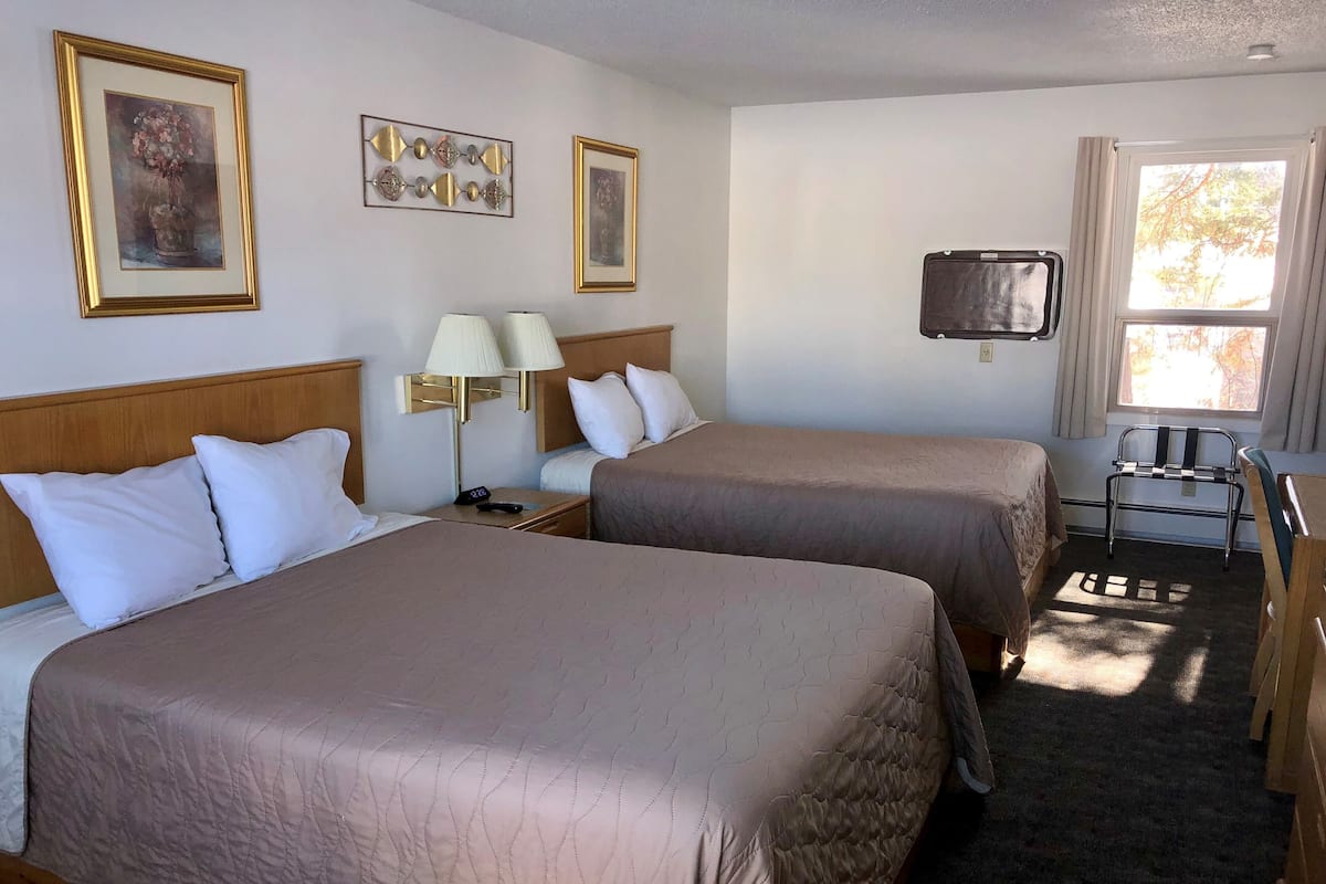 Habitación de hotel con dos camas, un escritorio, una silla, televisión y obras de arte en las paredes.