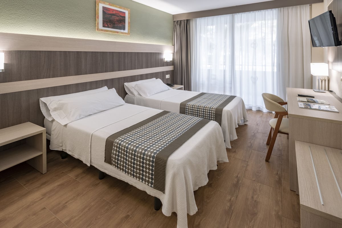 A hotel room with two beds, a desk, a chair, a television, and a window with curtains.