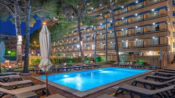 A hotel with a swimming pool surrounded by lounge chairs and umbrellas.