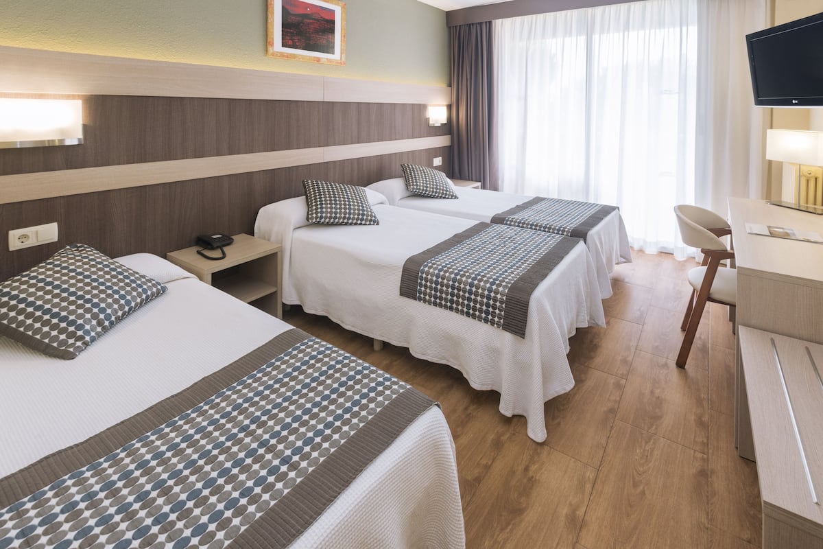 A hotel room with two beds, a desk, a chair, a TV, and a window with curtains.
