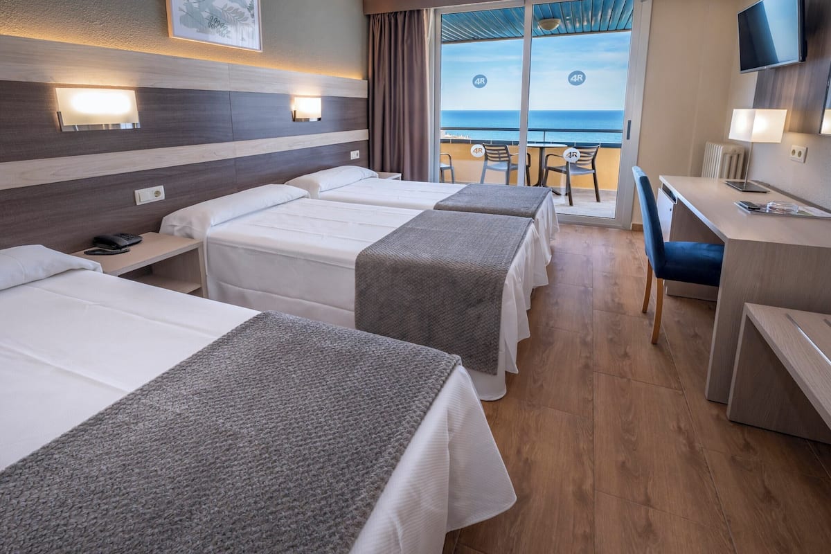A hotel room with three beds, a desk, a chair, and a TV.