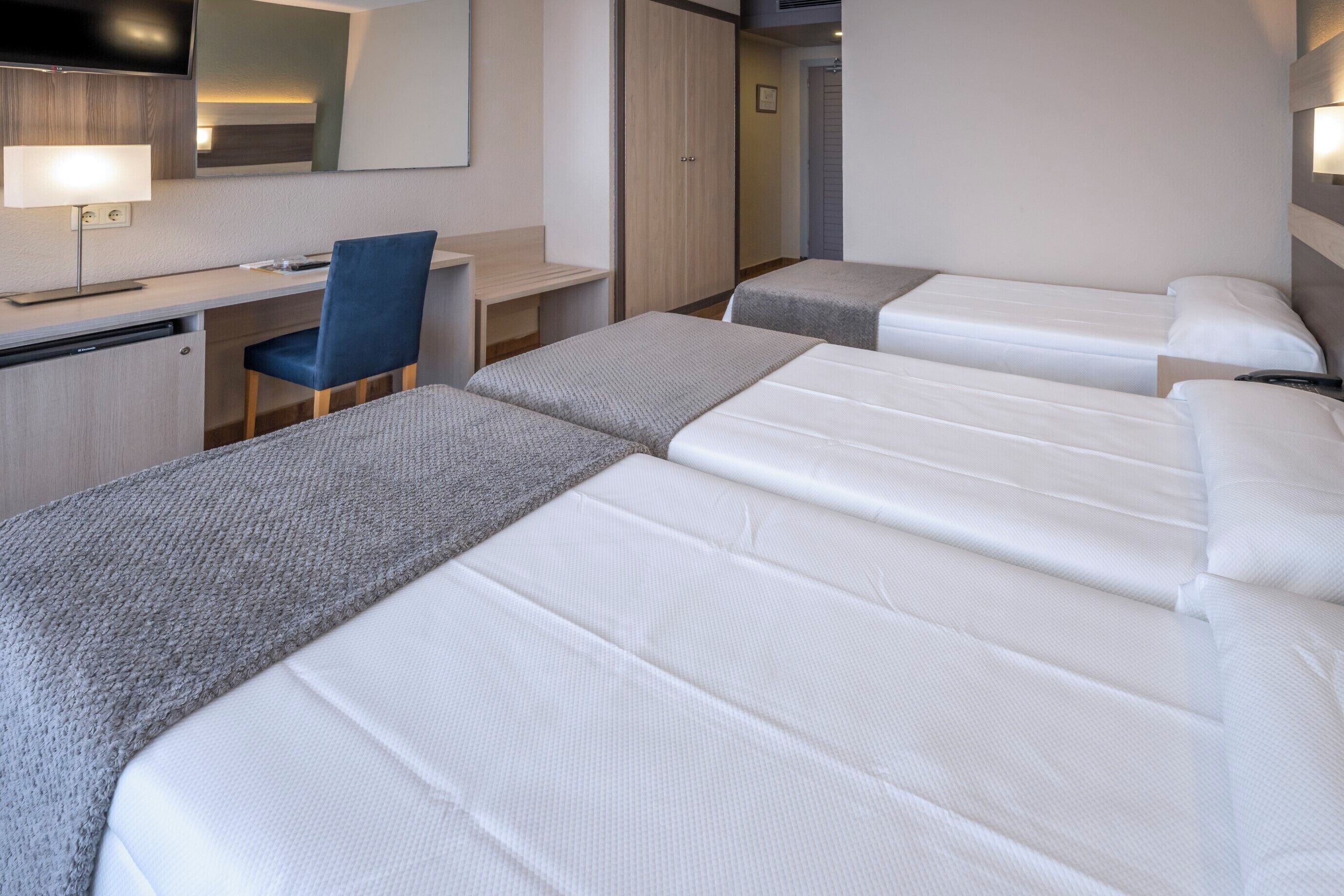 Une chambre d’hôtel avec deux lits, un bureau, une chaise et une télévision.