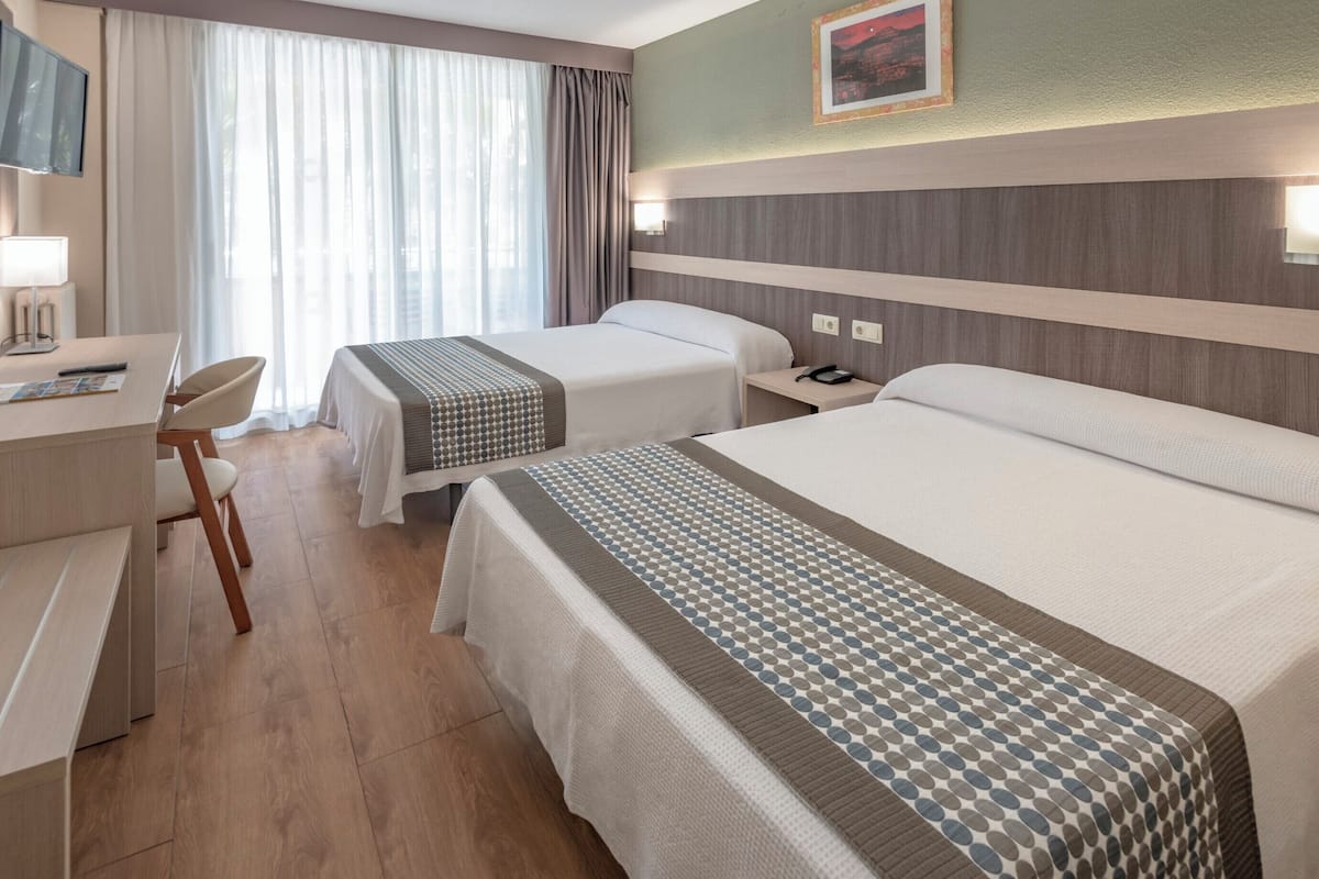 A hotel room with two beds, a desk, and a chair.