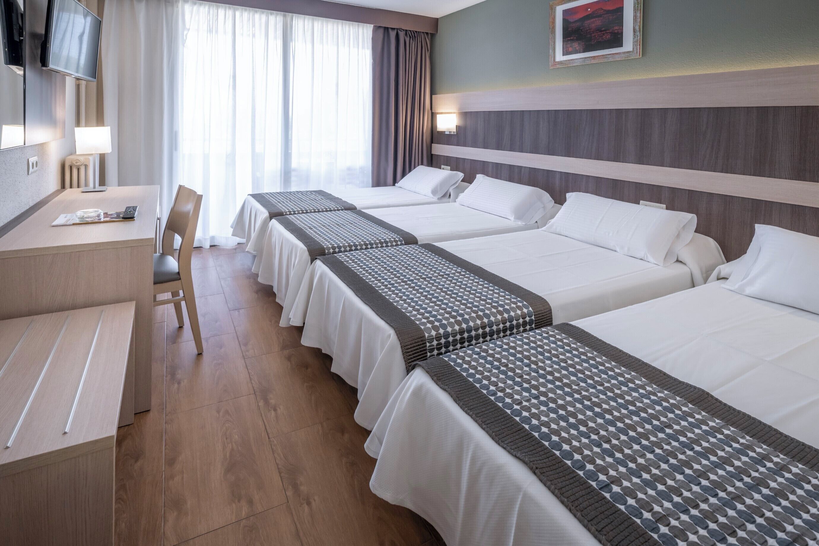Una camera d'albergo con tre letti, una scrivania, una sedia e una televisione.