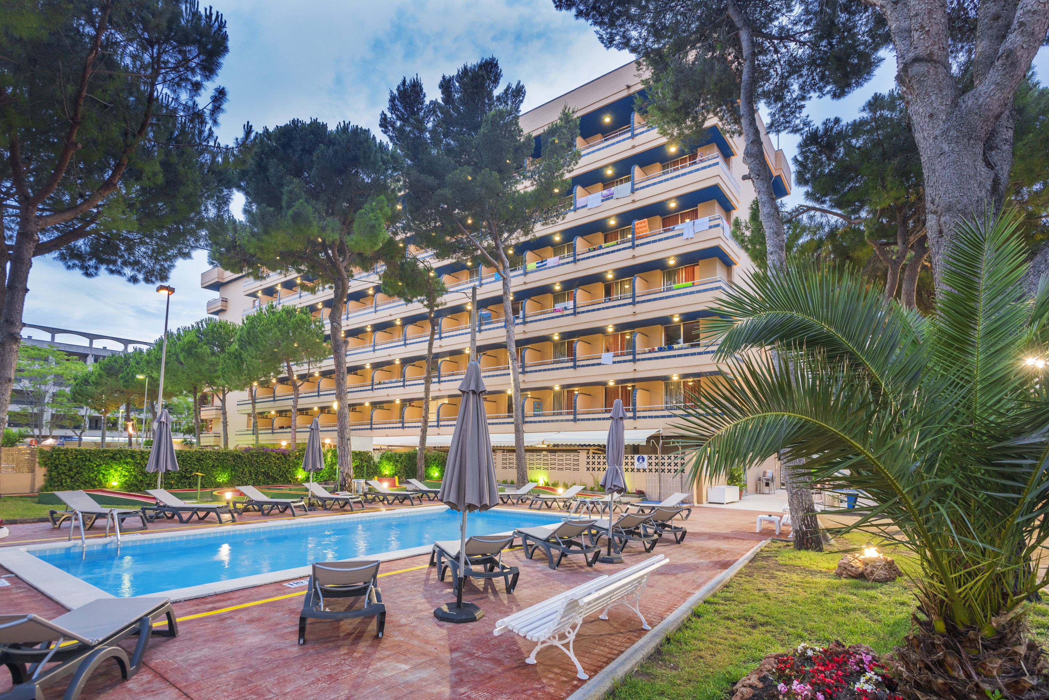Un hotel con zona de piscina, varios balcones y mobiliario exterior.