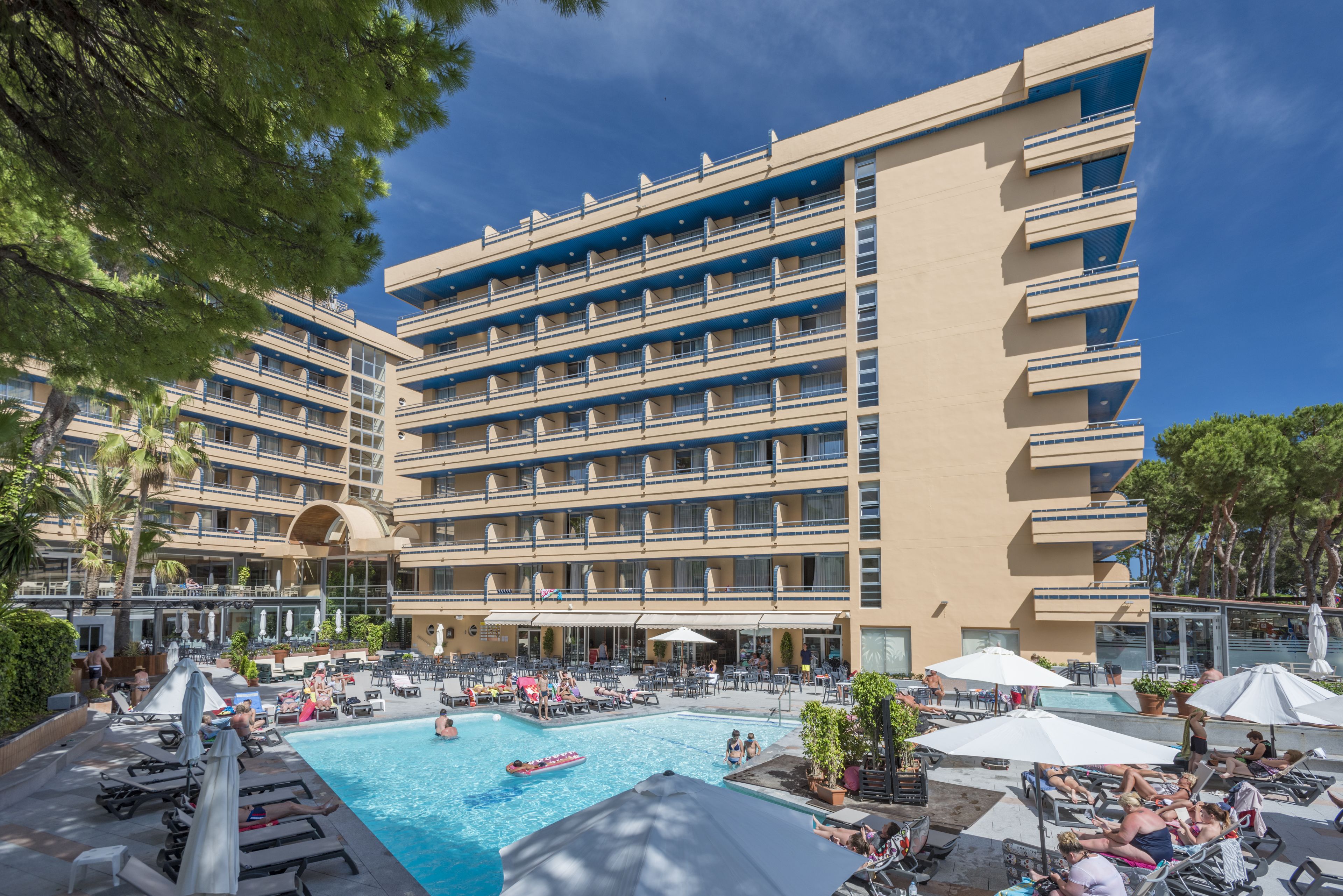 A hotel with multiple balconies, a swimming pool, and outdoor seating areas.