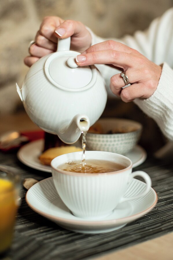 A person pouring tea from a white teapot into a white cup on a saucer. - Hotel de Lille (Paris)