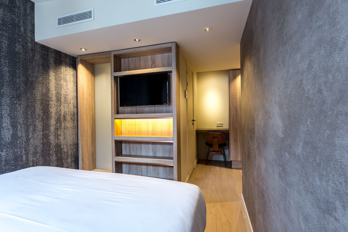 A modern hotel room with a bed, built-in shelving, and a small seating area.