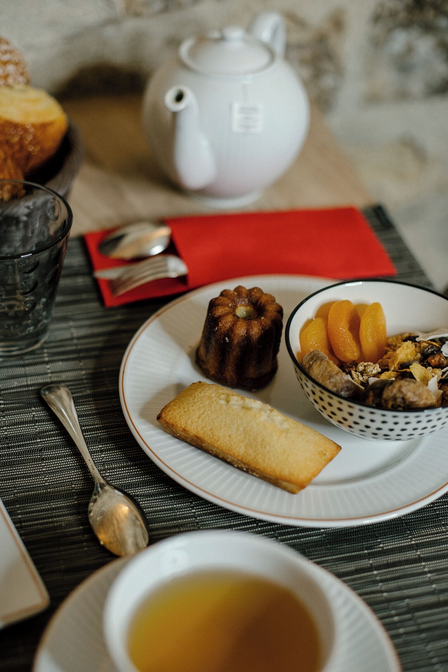 Una mesa con una tetera, un cuenco de fruta, una galleta y una taza de té.