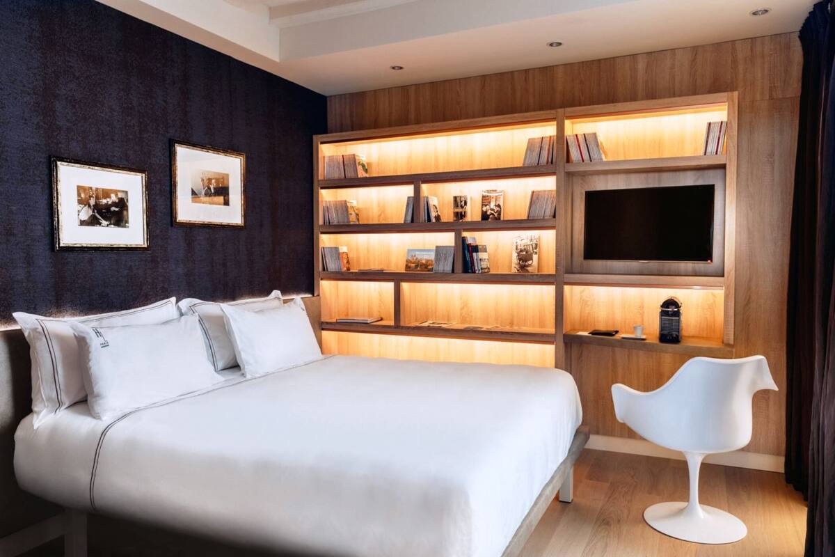 A modern bedroom with a large bed, a built-in bookshelf, a flat-screen TV, and a unique white chair.