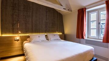 A neatly made bed with a headboard, a bedside table, and a window with curtains.
