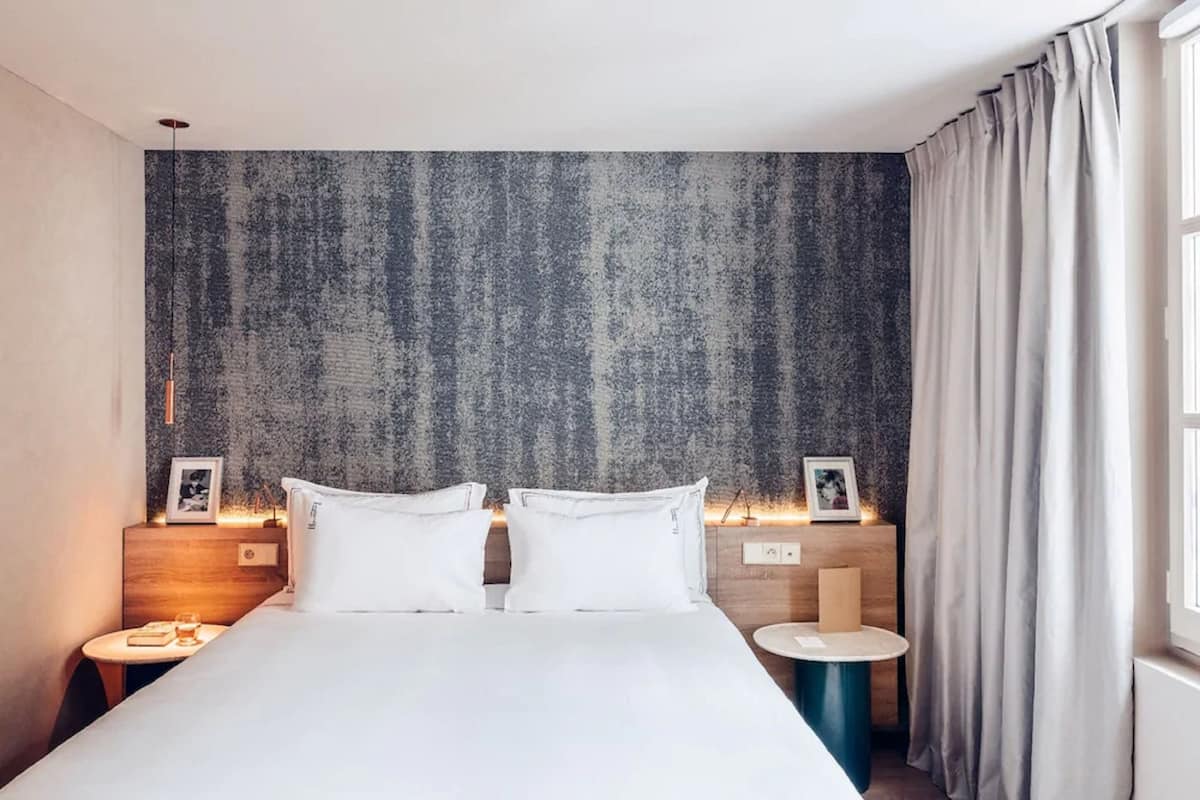 A modern hotel room with a large bed, two bedside tables, a small round table, and a textured wall.