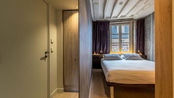 Un dormitorio con un armario de madera, una cama con ropa de cama blanca y una ventana con cortinas.
