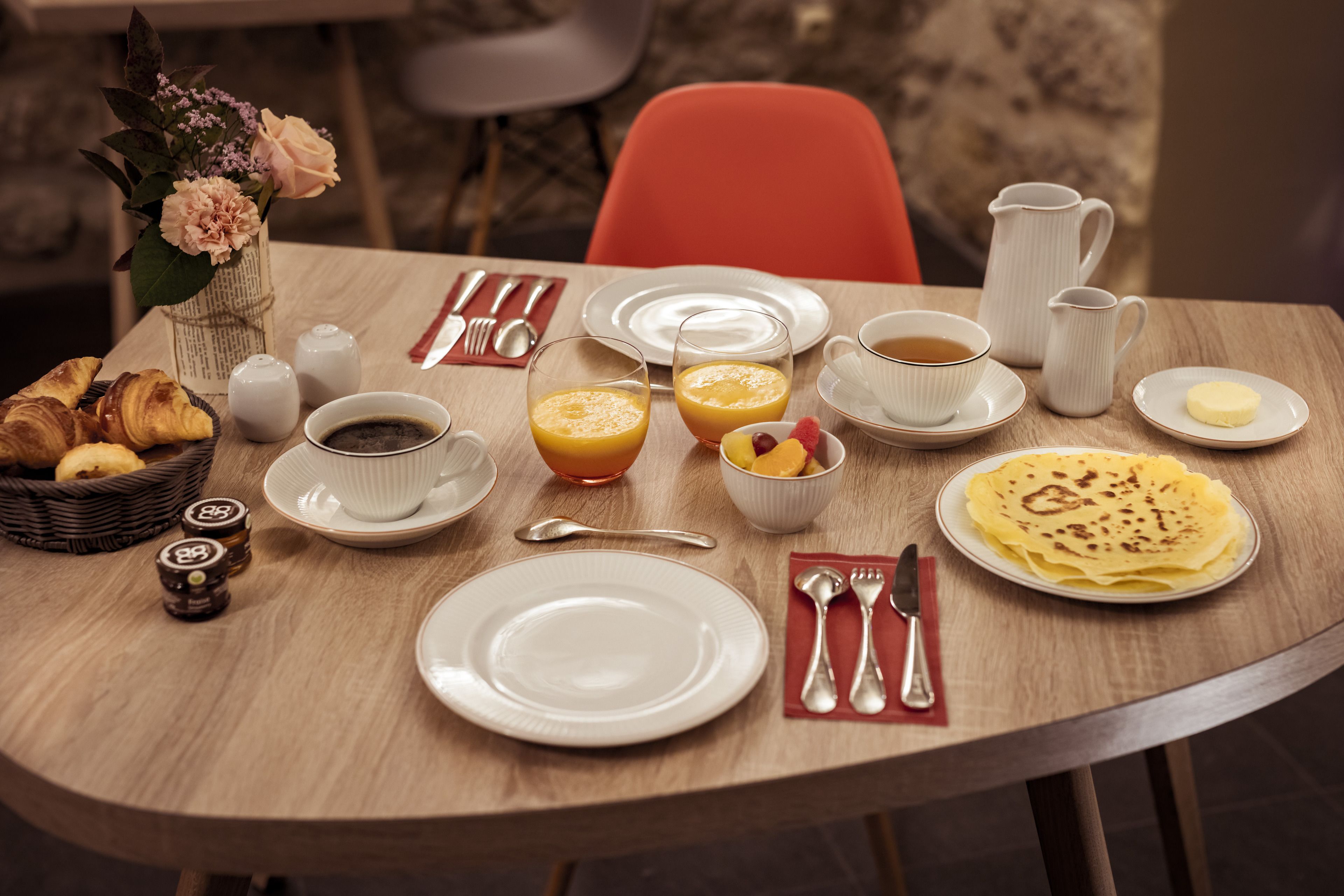 A breakfast table with croissants, orange juice, coffee, a pitcher, and a plate of pancakes.