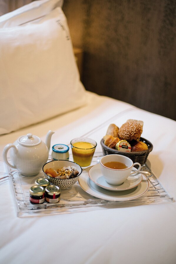 Un desayuno preparado sobre la cama, con un hervidor de agua, tazas, un cuenco de fruta, una cesta de pasteles y frascos de mermelada.