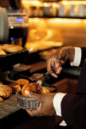 A person using tongs to handle food items, likely in a buffet setting. - Hotel de Lille (Paris)
