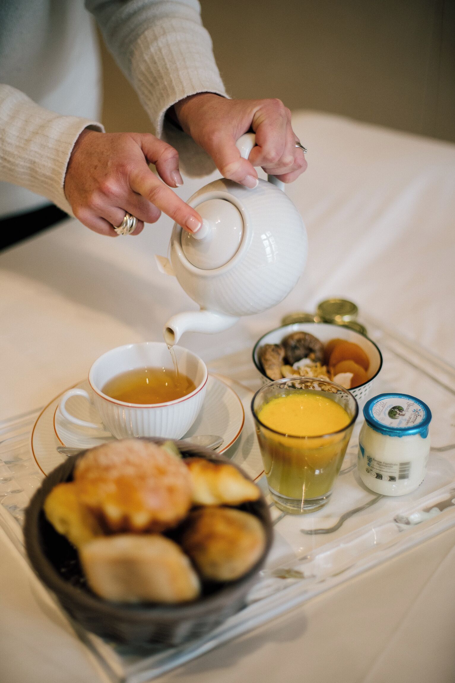 Una bandeja con una taza de té, un vaso de jugo y un bol de pasteles sobre una mesa.