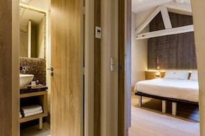 A hotel room with a wooden door, a bathroom with a sink and mirror, and a bed with a headboard. - Hotel de Lille (Paris)
