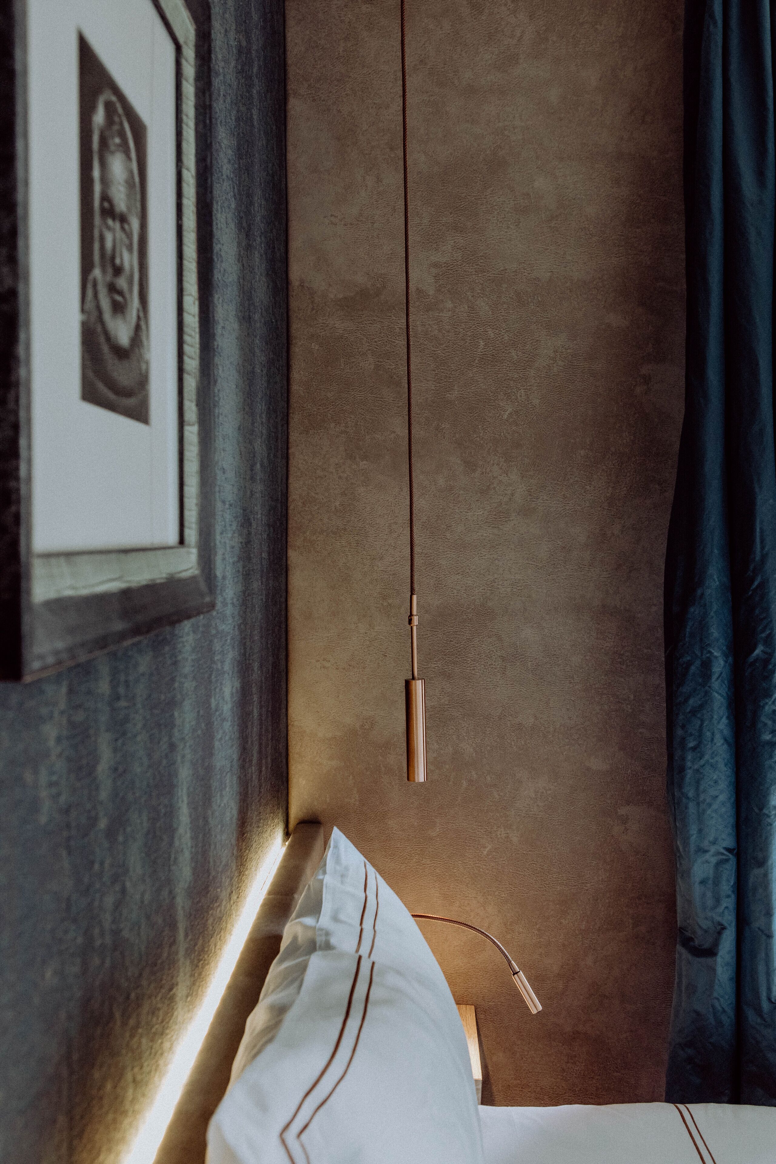 A modern bedroom with a bed, a framed picture on the wall, and a hanging light fixture.