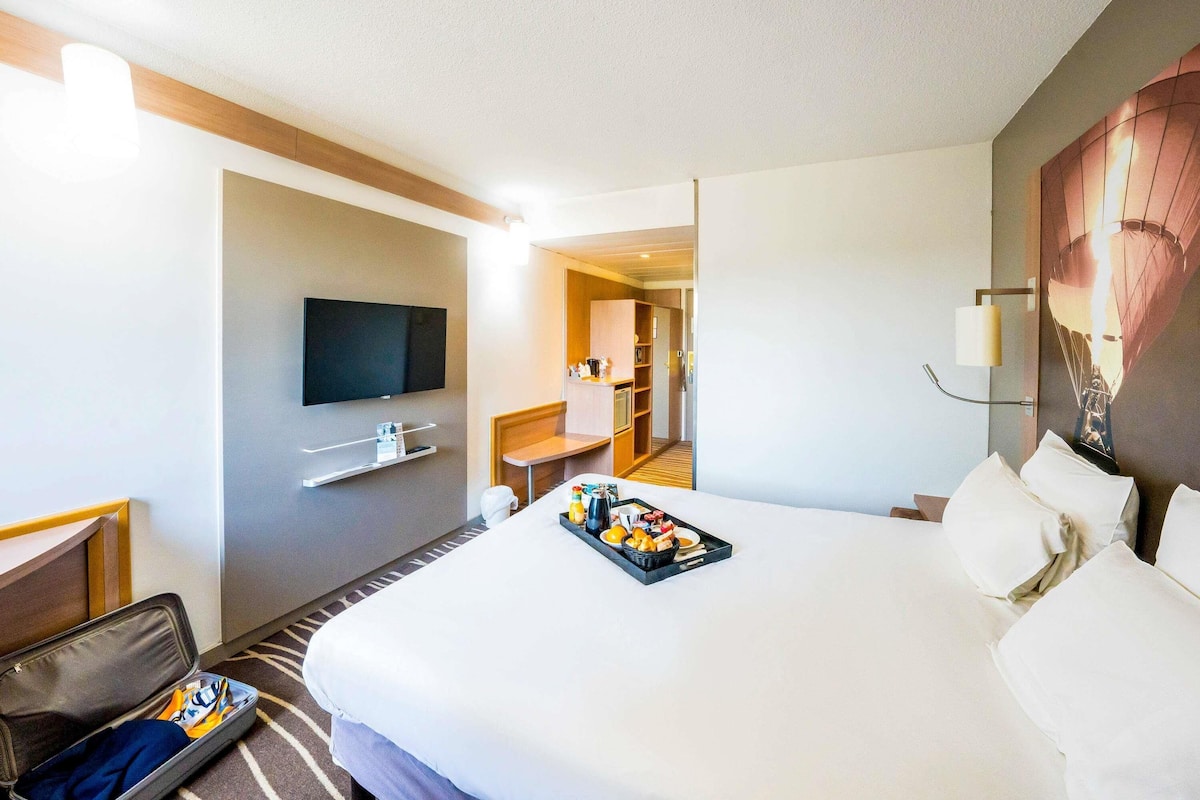 Habitación de hotel con cama, televisión, escritorio y baño visible a través de una puerta abierta.