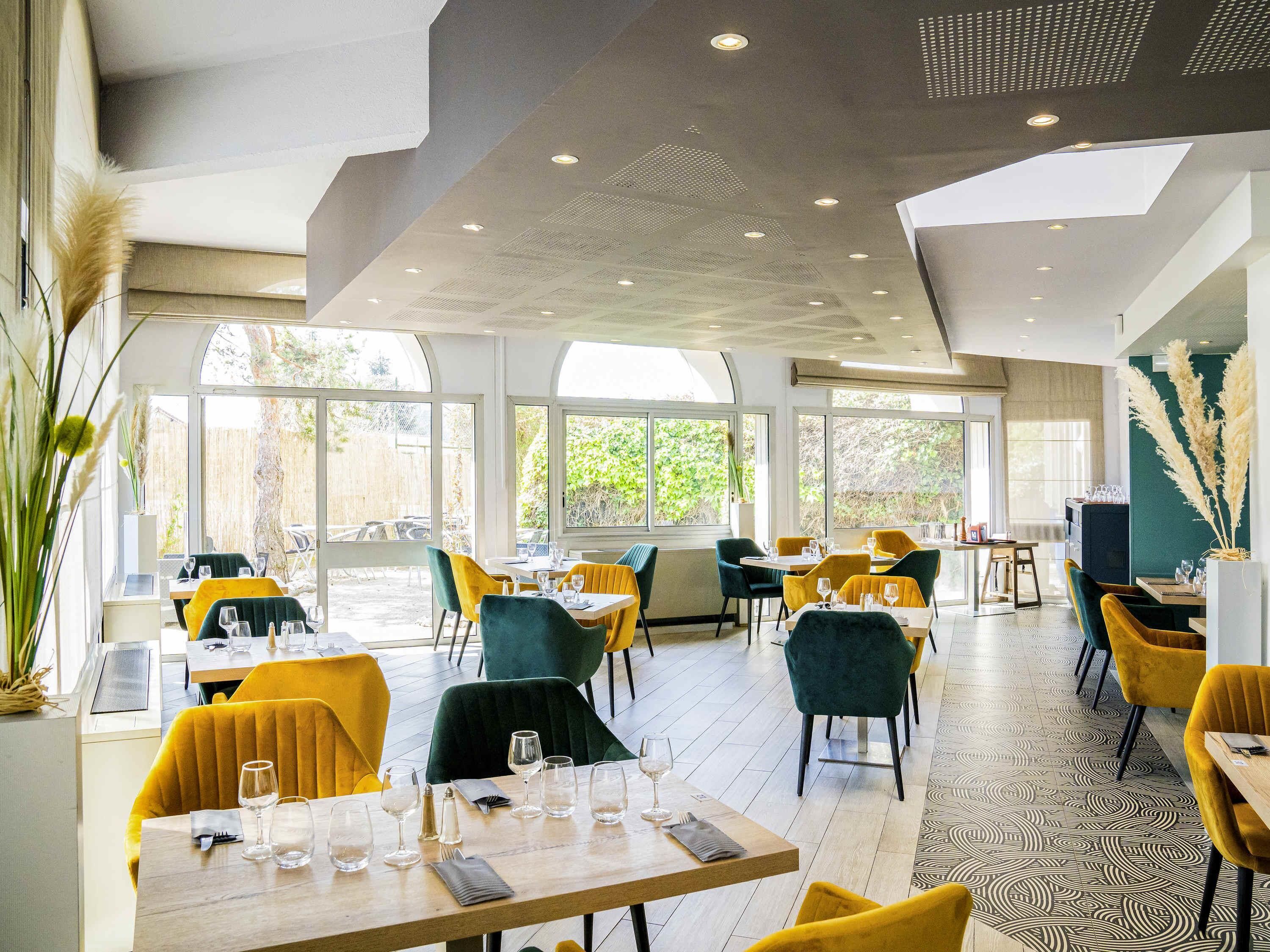 En restaurant med dækketøjet borde, store vinduer og et moderne loftsdesign.