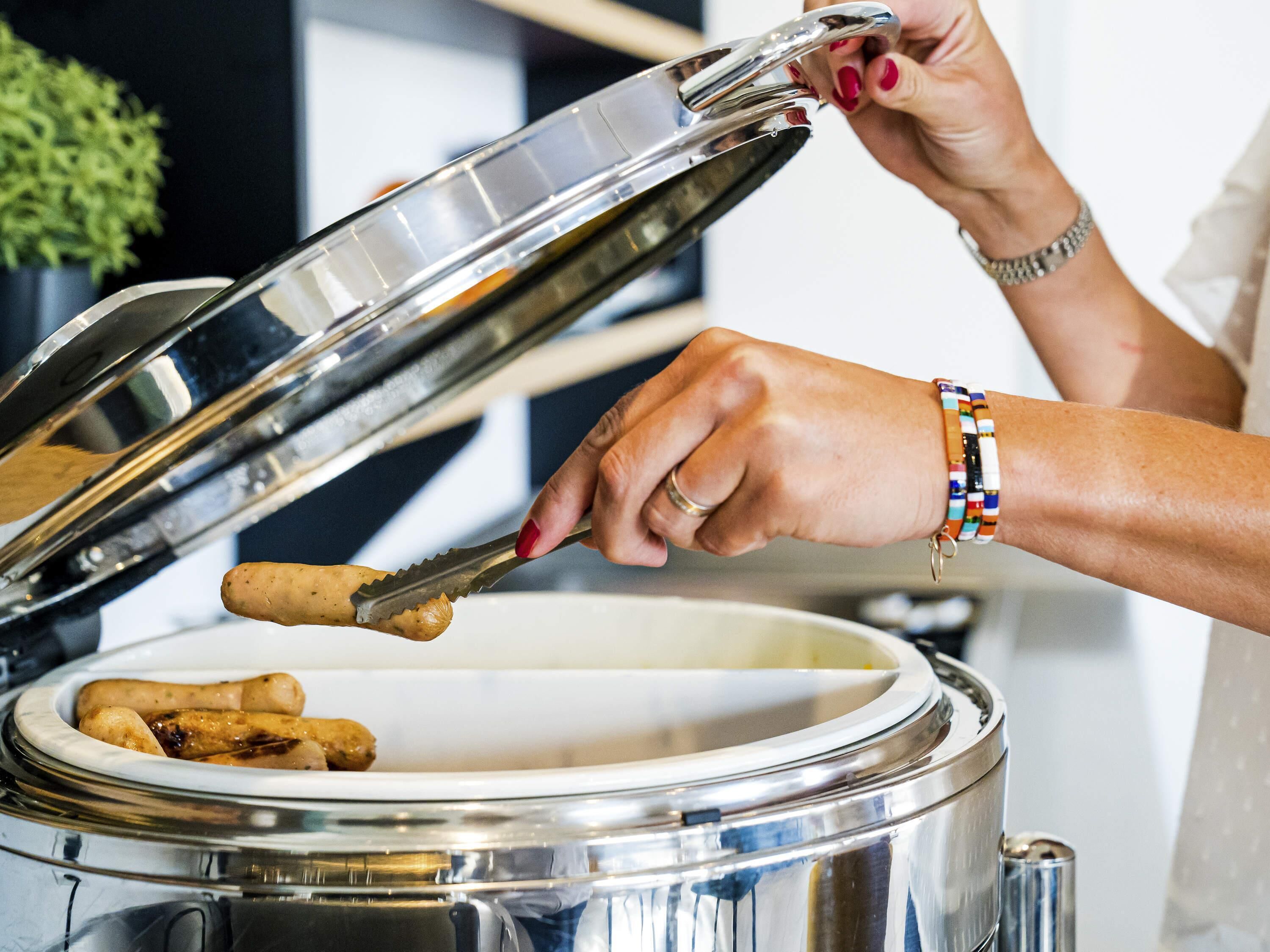 A person opening a stainless steel pot with a lid.