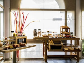 A bakery display with pastries and bread, a coffee station, and a view of the street through large windows.