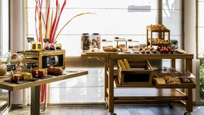 Mostrador de panadería con pasteles y pan, una estación de café y vista a la calle a través de amplias ventanas.