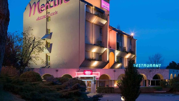 Un hotel llamado 'Mercure' con un cartel que indica 'restaurante', con un diseño arquitectónico moderno, múltiples balcones y una entrada bien iluminada.