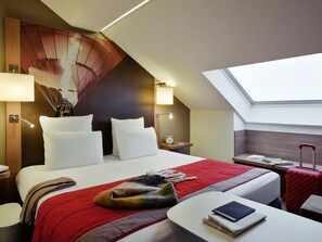 A hotel room with a bed, a desk, a chair, a lamp, a clock, and a window.