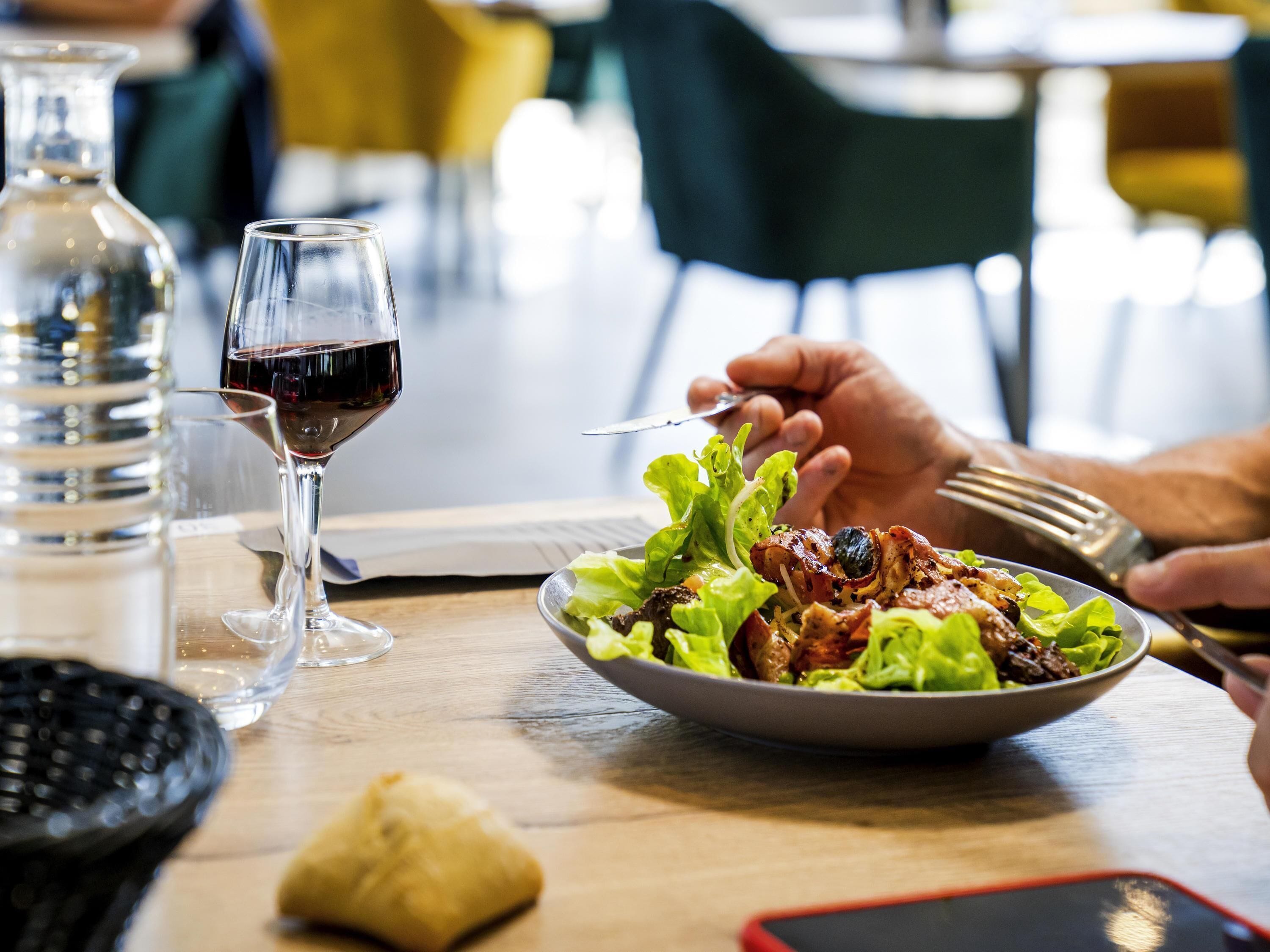 Une table à manger avec une assiette de nourriture, un verre de vin rouge et une bouteille.