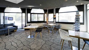 Un interior moderno con suelo de patrón geométrico, una zona de estar con mesa y sillas, y ventanas amplias que dejan entrar luz natural.