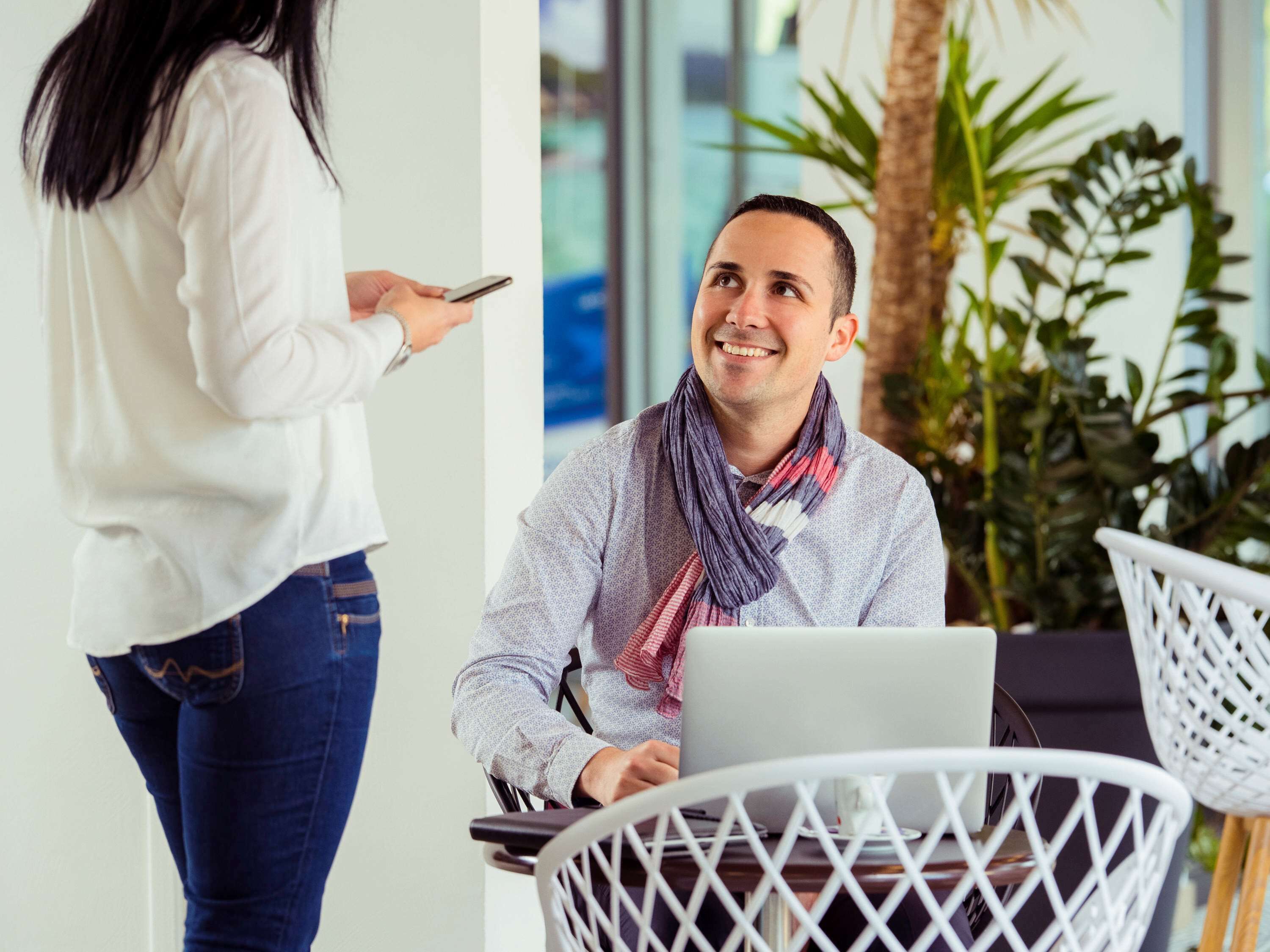 A person using a laptop in a modern office setting with white furniture and indoor plants.
