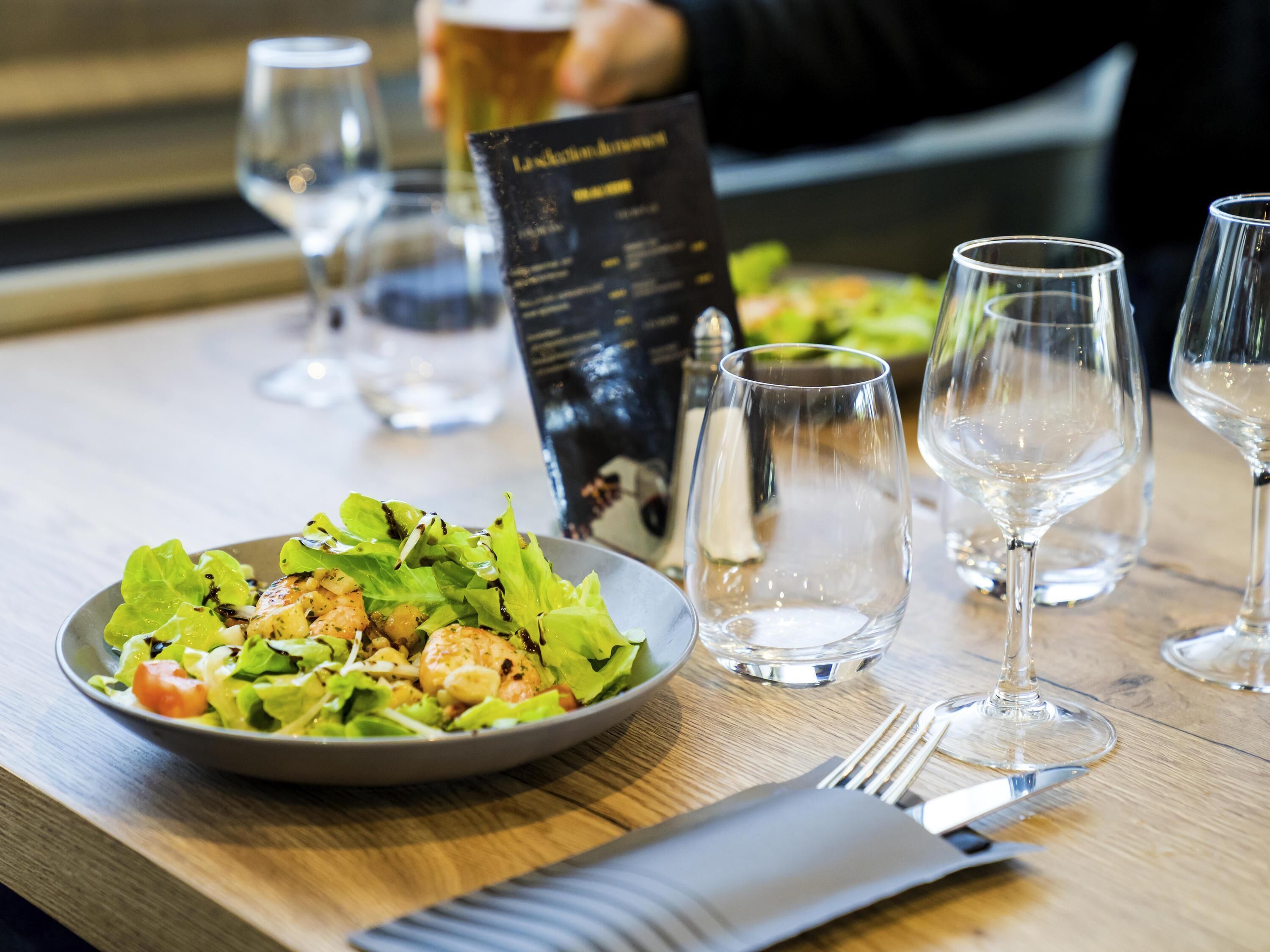 A dining table with a plate of salad, empty wine glasses, and a menu.