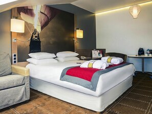 Ein Hotelzimmer mit einem großen Bett, einem Sessel, einem Schreibtisch und einer Wandlampe.