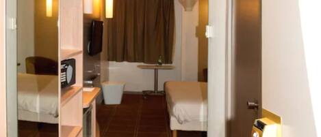 A hotel room with a bed, a desk, a chair, a small table, a mirror, and a door with a light switch.