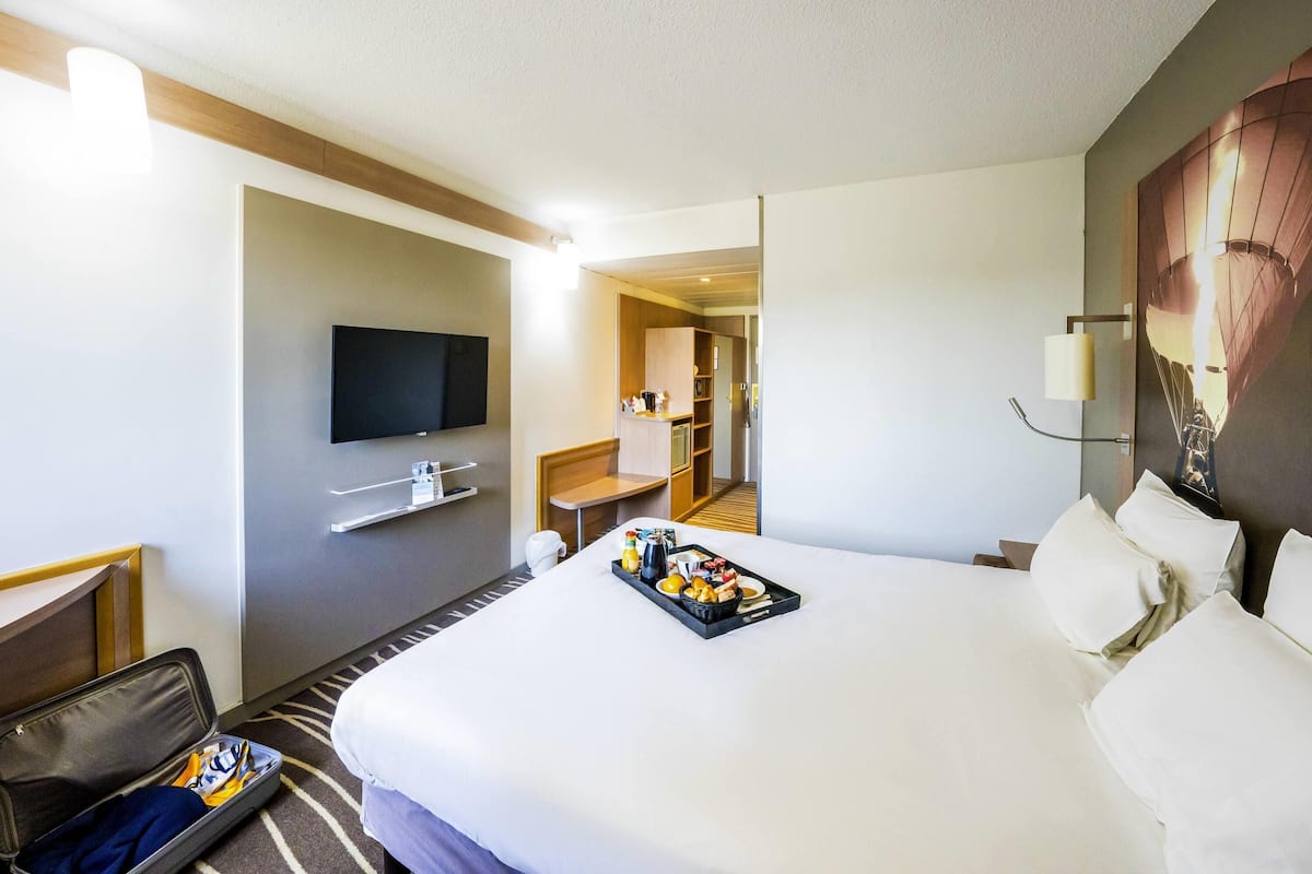 A hotel room with a bed, a flat-screen TV, a desk, and a tray of breakfast items.