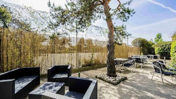 An outdoor seating area with black woven furniture, a tree, and a bamboo fence.