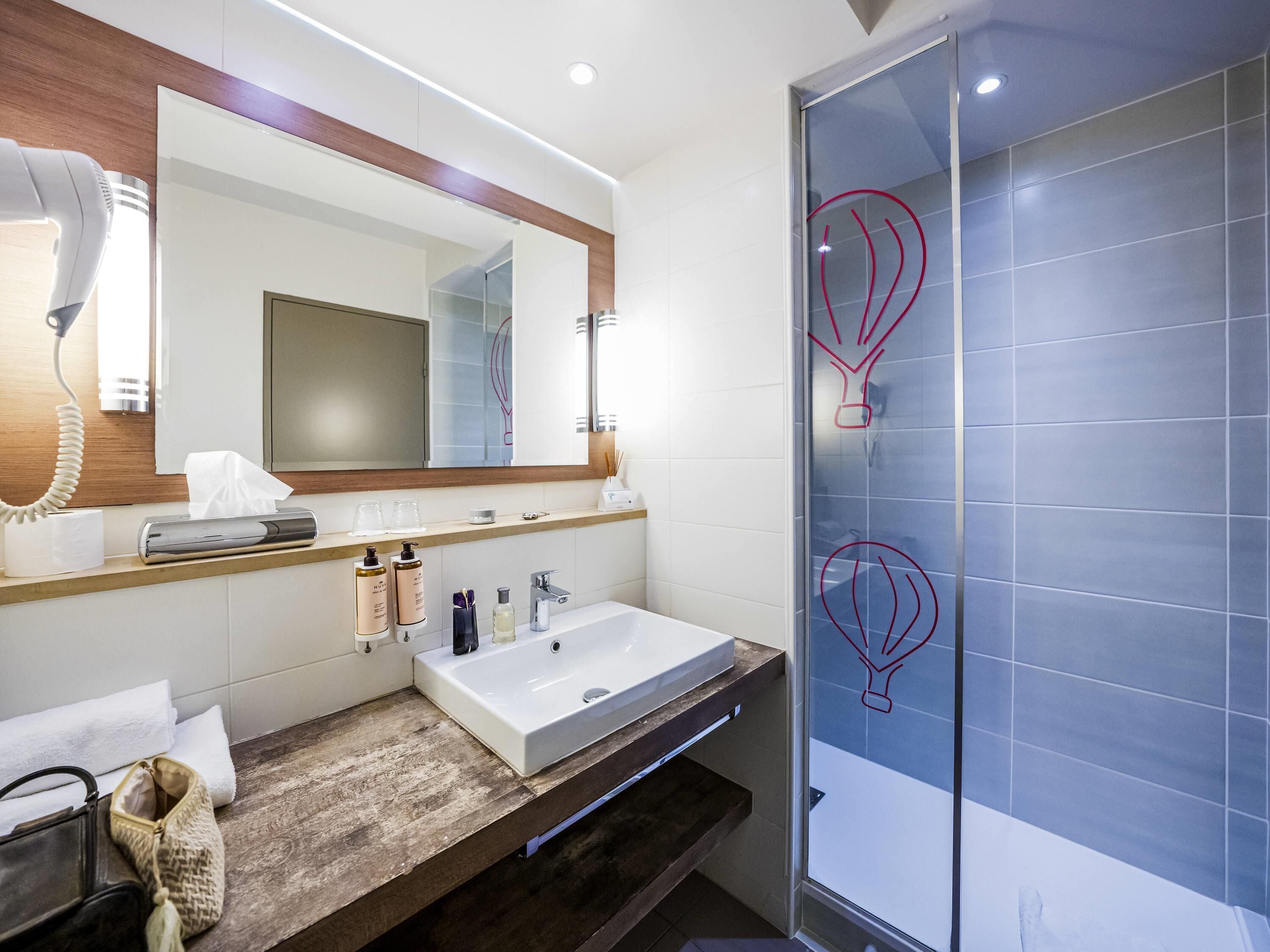 A modern bathroom with a large mirror, a sink, a towel rack, and a glass shower enclosure.