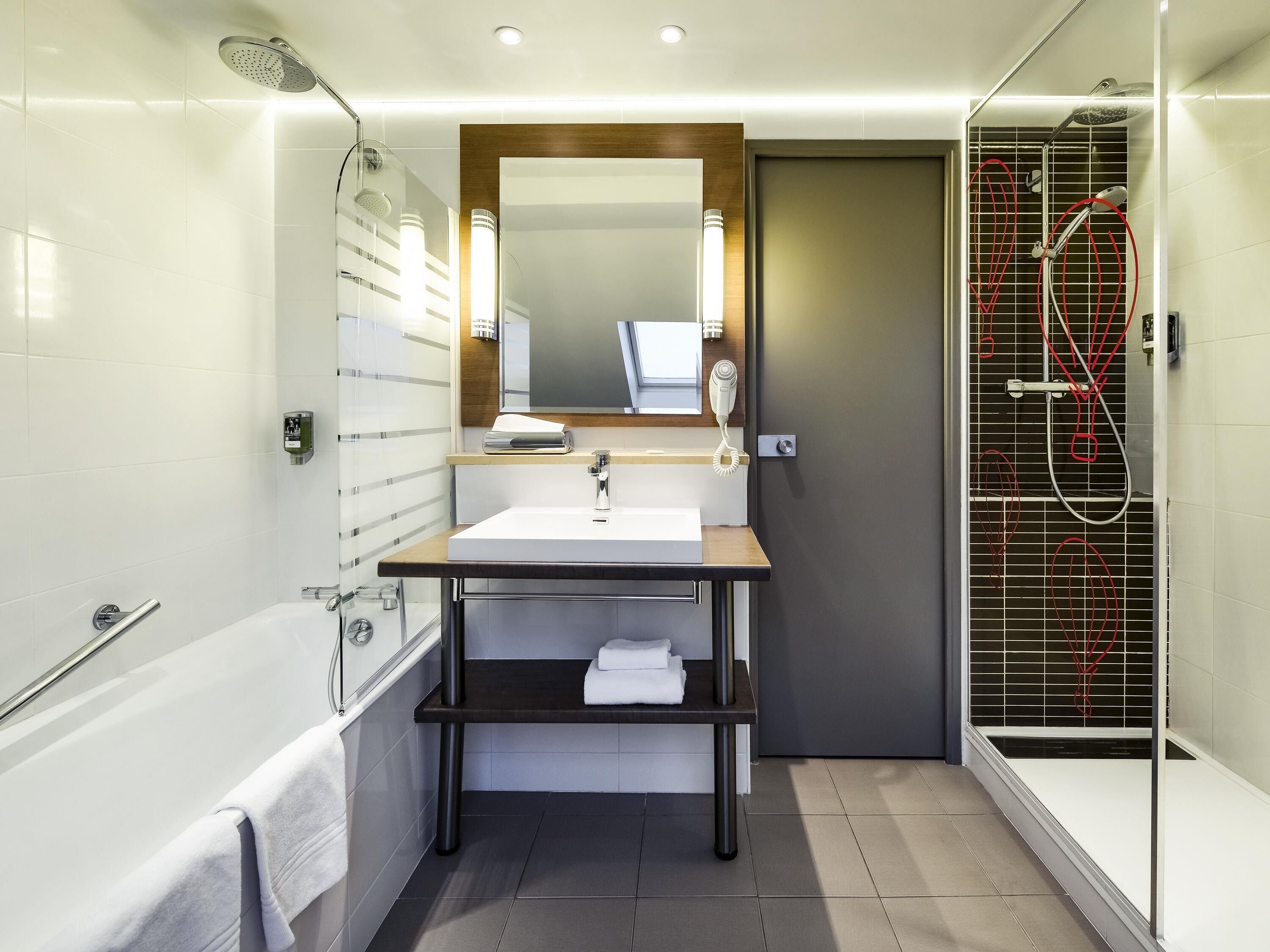 Ein modernes Badezimmer mit Badewanne, Waschbecken inklusive Spiegel, Handtuchhalter und Dusche mit Glastür.