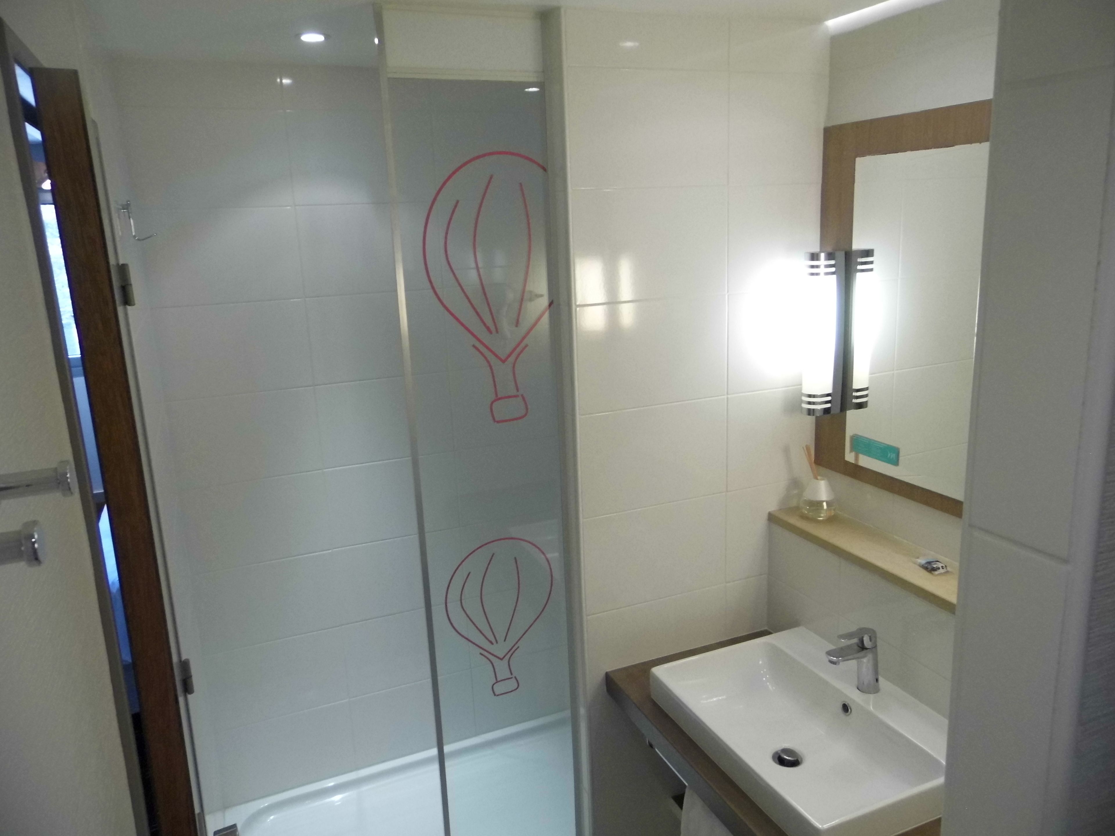 A modern bathroom with a glass shower door, a white sink, and a mirror.