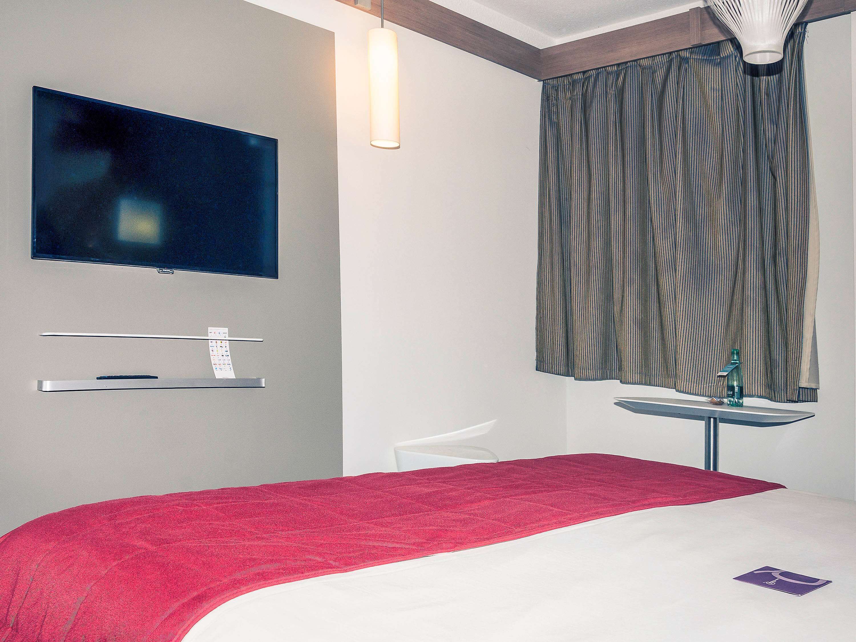 Ein Hotelzimmer mit Bett, Wandfernseher, kleinem Tisch mit Flasche und Stuhl.
