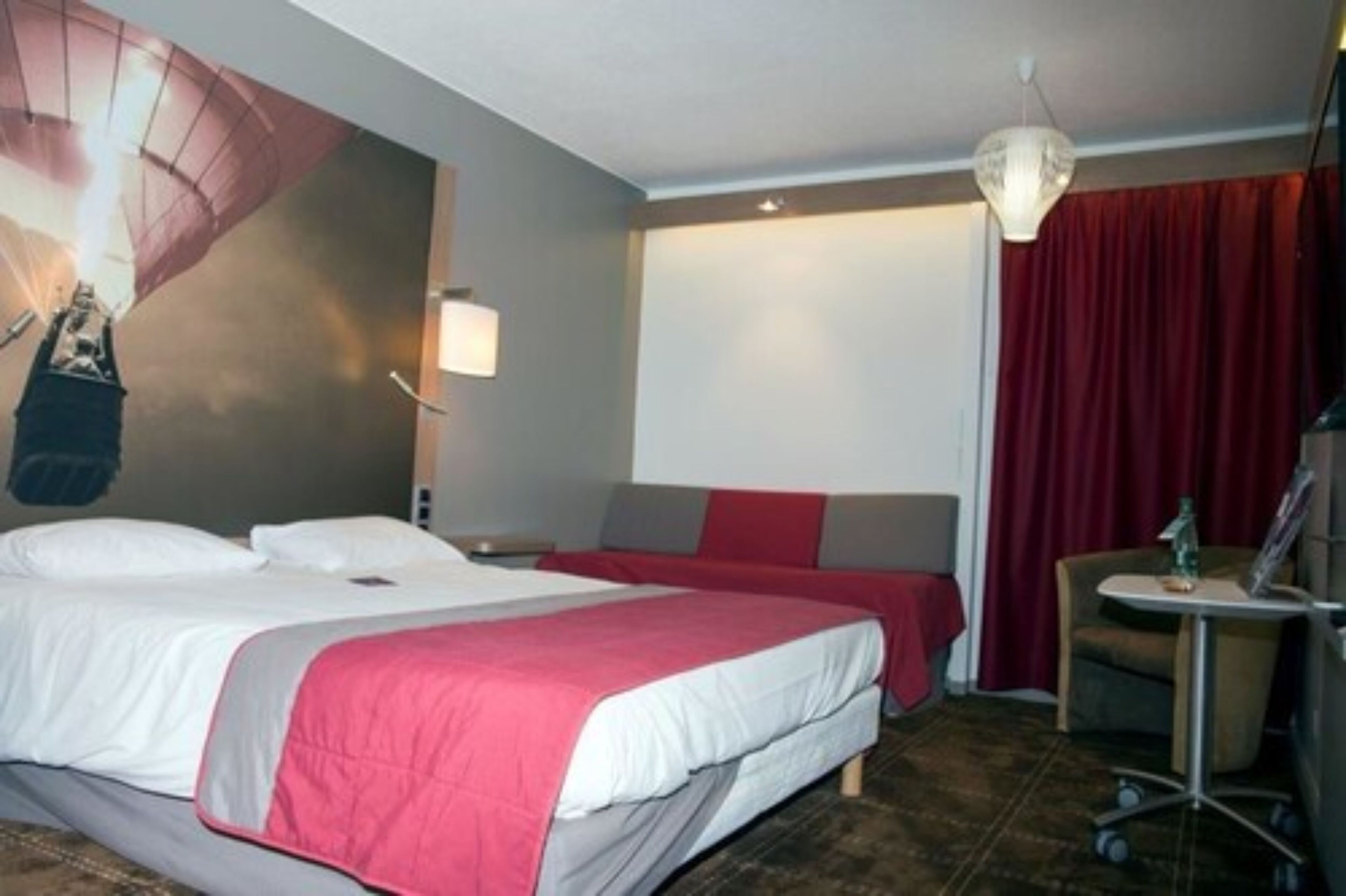 Quarto de hotel com uma cama grande, uma cama menor, uma escrivaninha e uma cadeira.