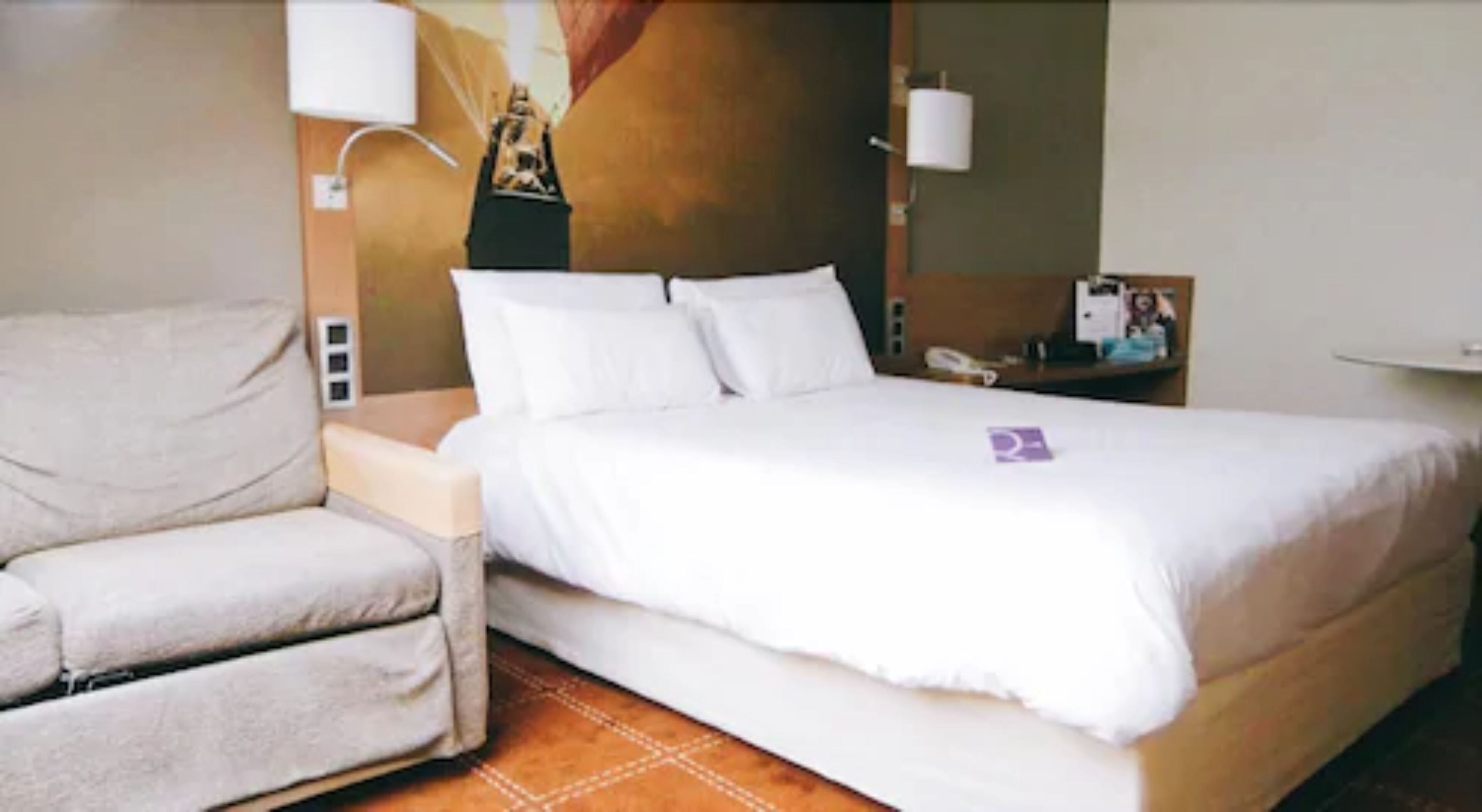 Una habitación de hotel con cama, una silla, un escritorio y un teléfono en la pared.