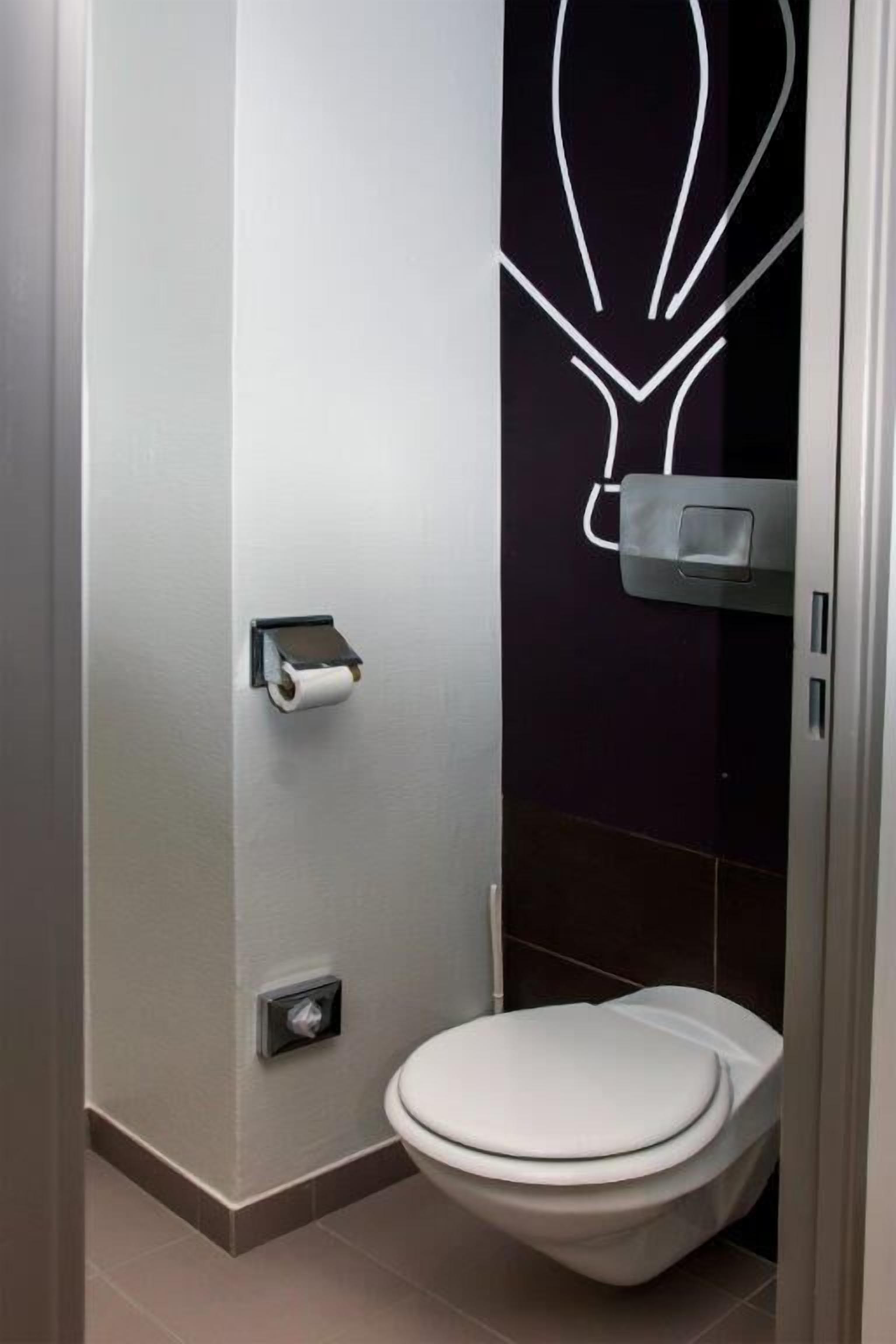A modern bathroom with a toilet, a paper towel dispenser, and a hand dryer.