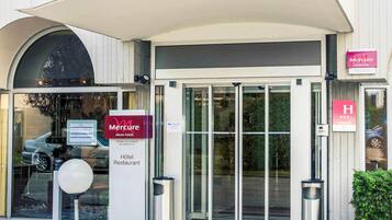 A Mercure Accor hotel entrance with a glass door, a sign indicating the hotel and restaurant, and a parking sign.