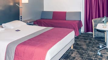 Et hotelværelse med to senge, et lille bord med en flaske og en stol.