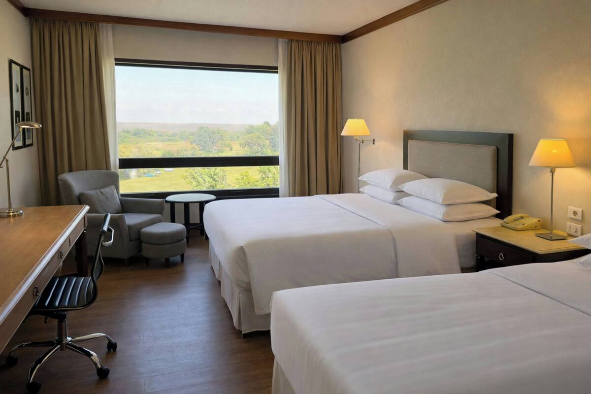 Habitación de hotel con dos camas, un escritorio, una silla y vista al exterior.