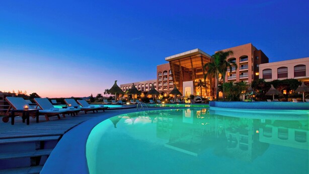A poolside area with lounge chairs, a pool, and a hotel building with multiple floors and balconies.